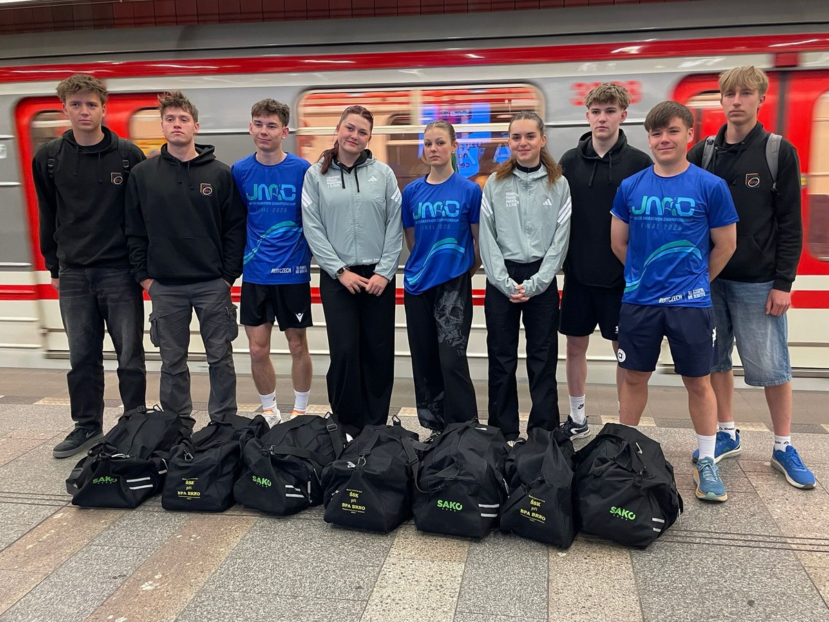 Mladí běžci v dresech Junior Marathon Championship stojí s taškami Sako na nástupišti metra.